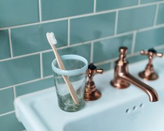 Wooden toothbrush in a glass on a white sink with copper taps and blue tiles