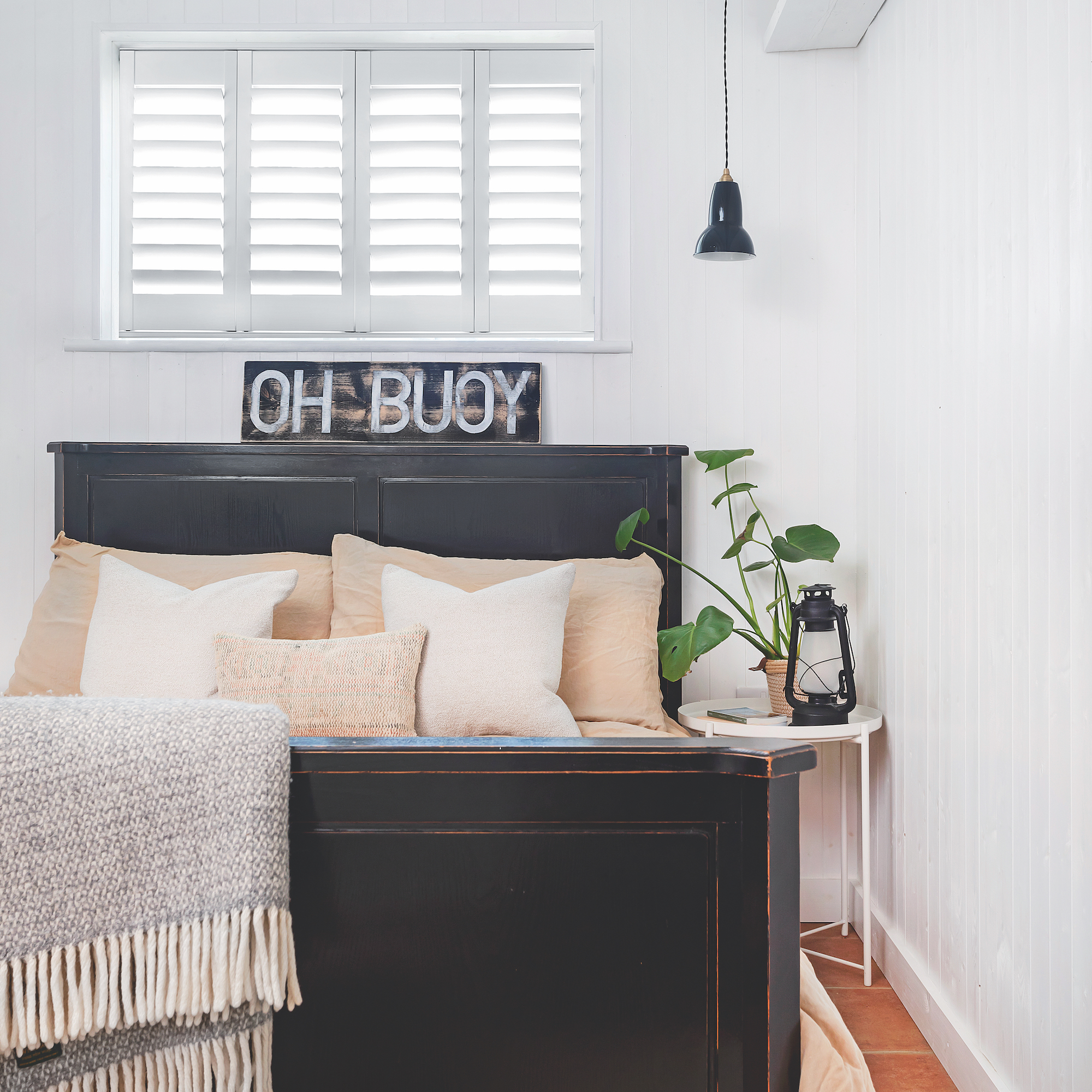 Coastal style bedroom with black wooden bed and white wood panel walls with vintage sign above bed