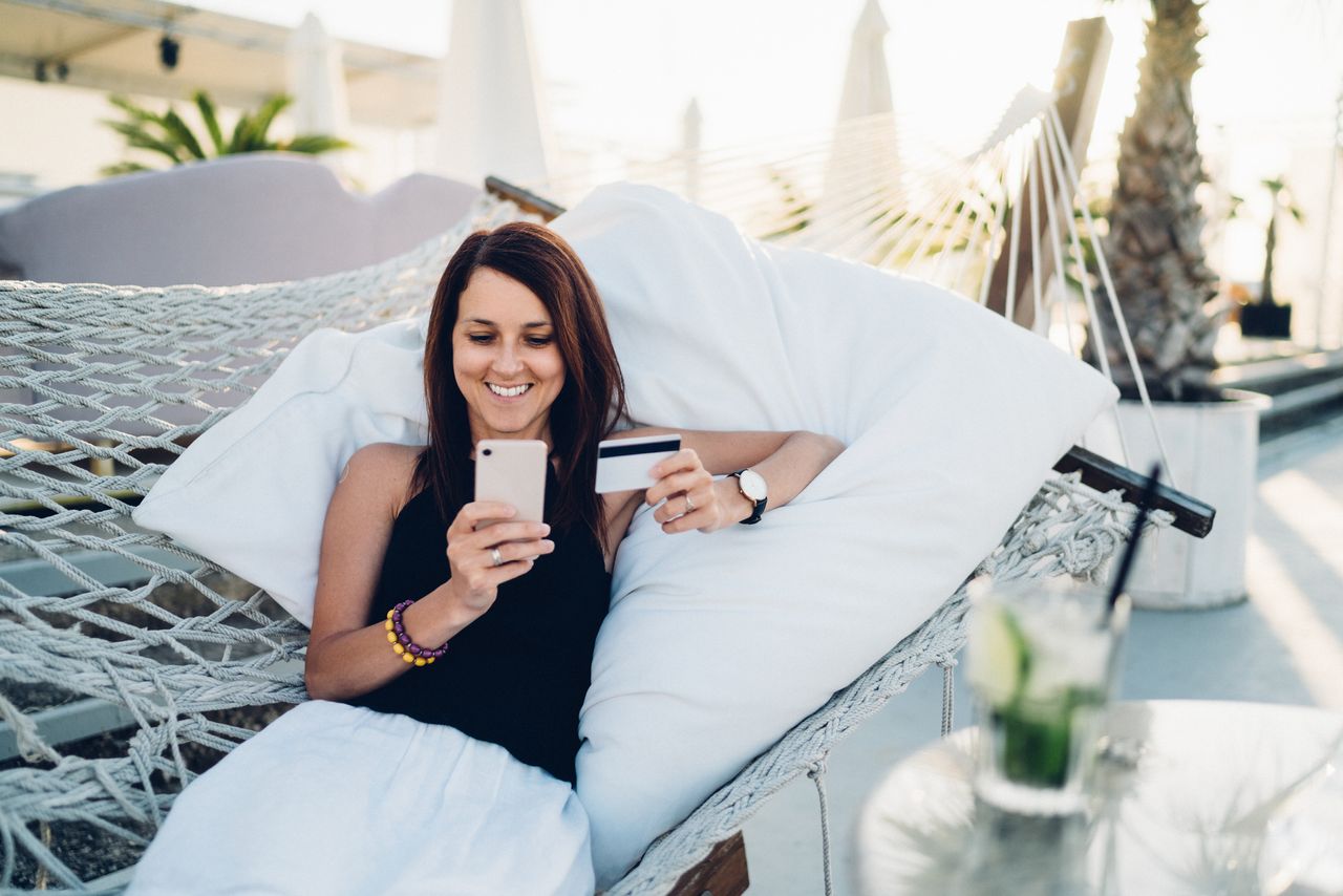 A woman shops onine while sitting in a hammock outdoors.