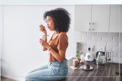 Woman sitting on kitchen worktop and eating a probiotic yoghurt