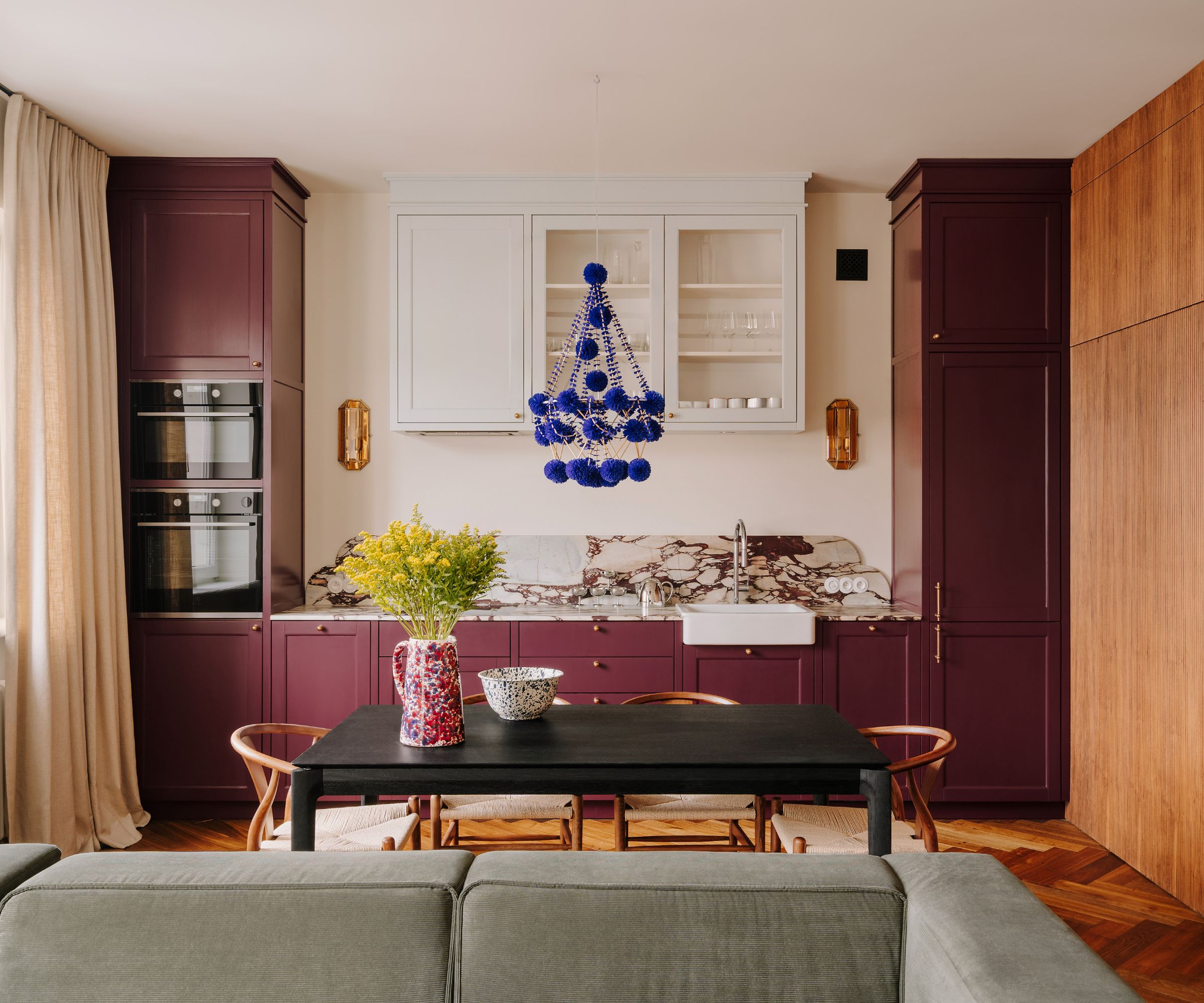 Open plan kitchen with aubergine painted cabinets, marble countertops, white cabinets and dining table with wooden chairs