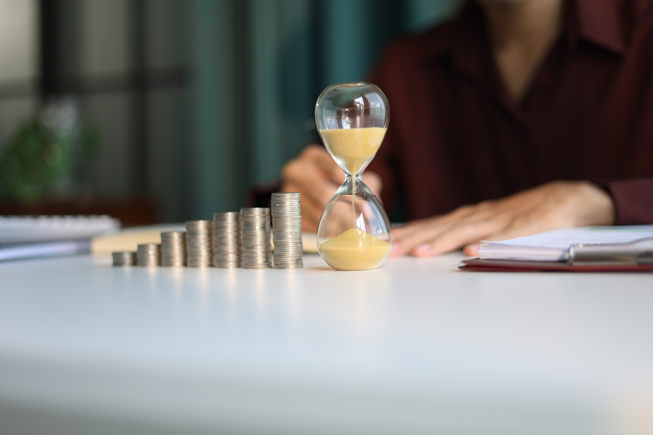 Rising stack of coins and hourglass representing long term investing through investment trusts