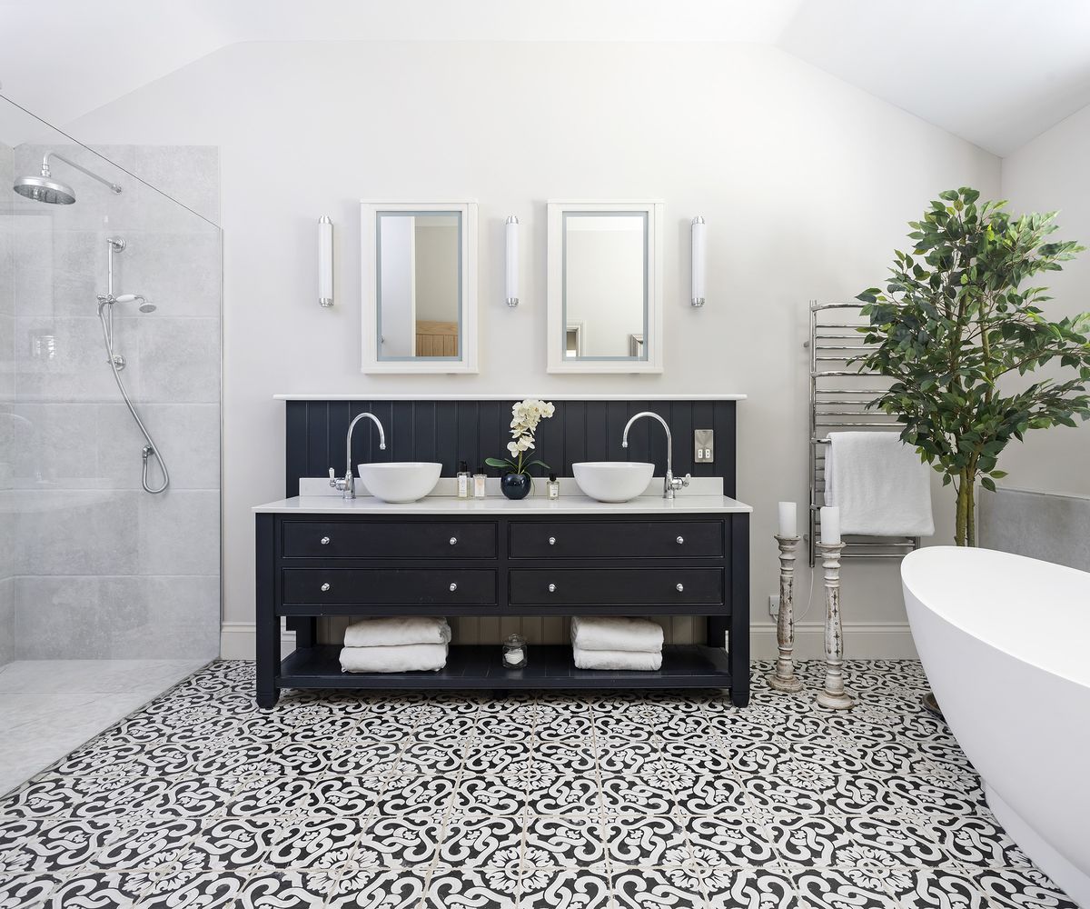 Twin sinks set into wooden bathroom cabinets with an ornate tiled floor and walk in shower