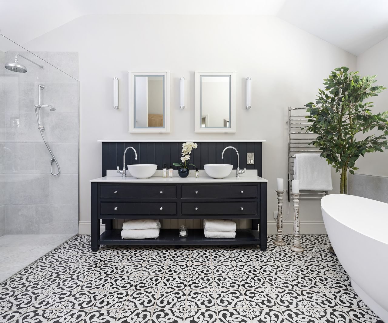 Twin sinks set into wooden bathroom cabinets with an ornate tiled floor and walk in shower