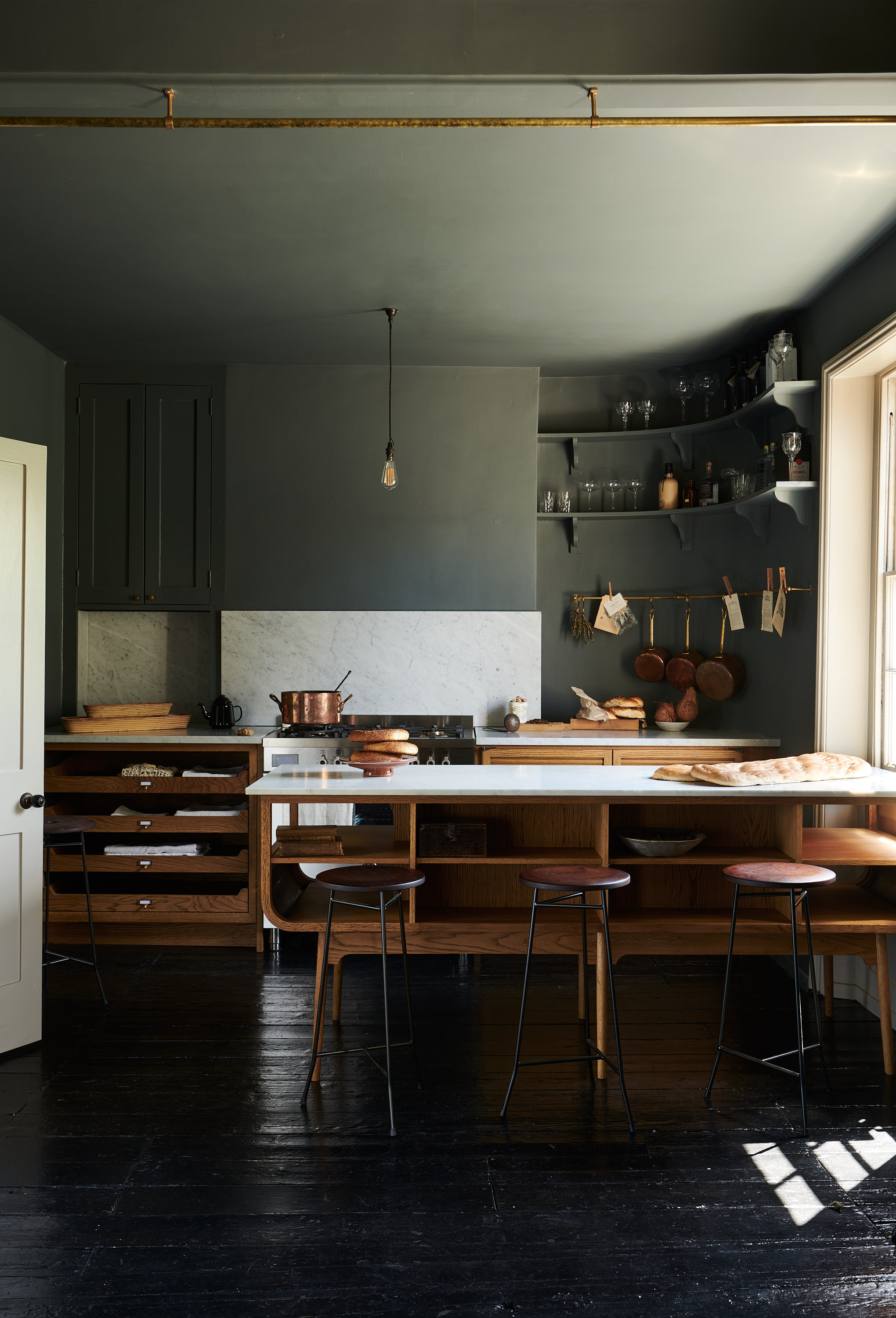 A kitchen in black wooden flooring, with wooden storage, a wooden peninsula with tall bar stools in front of it