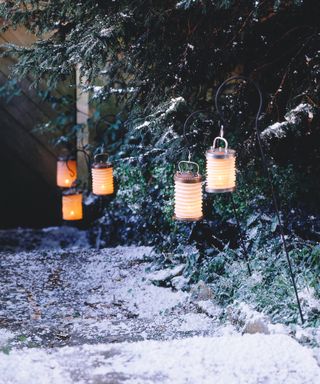 Orange garden lanterns in the snow arranged along a garden path