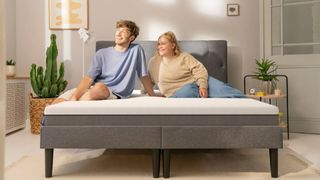 A couple sitting on the Emma Original memory foam mattress in a bedroom