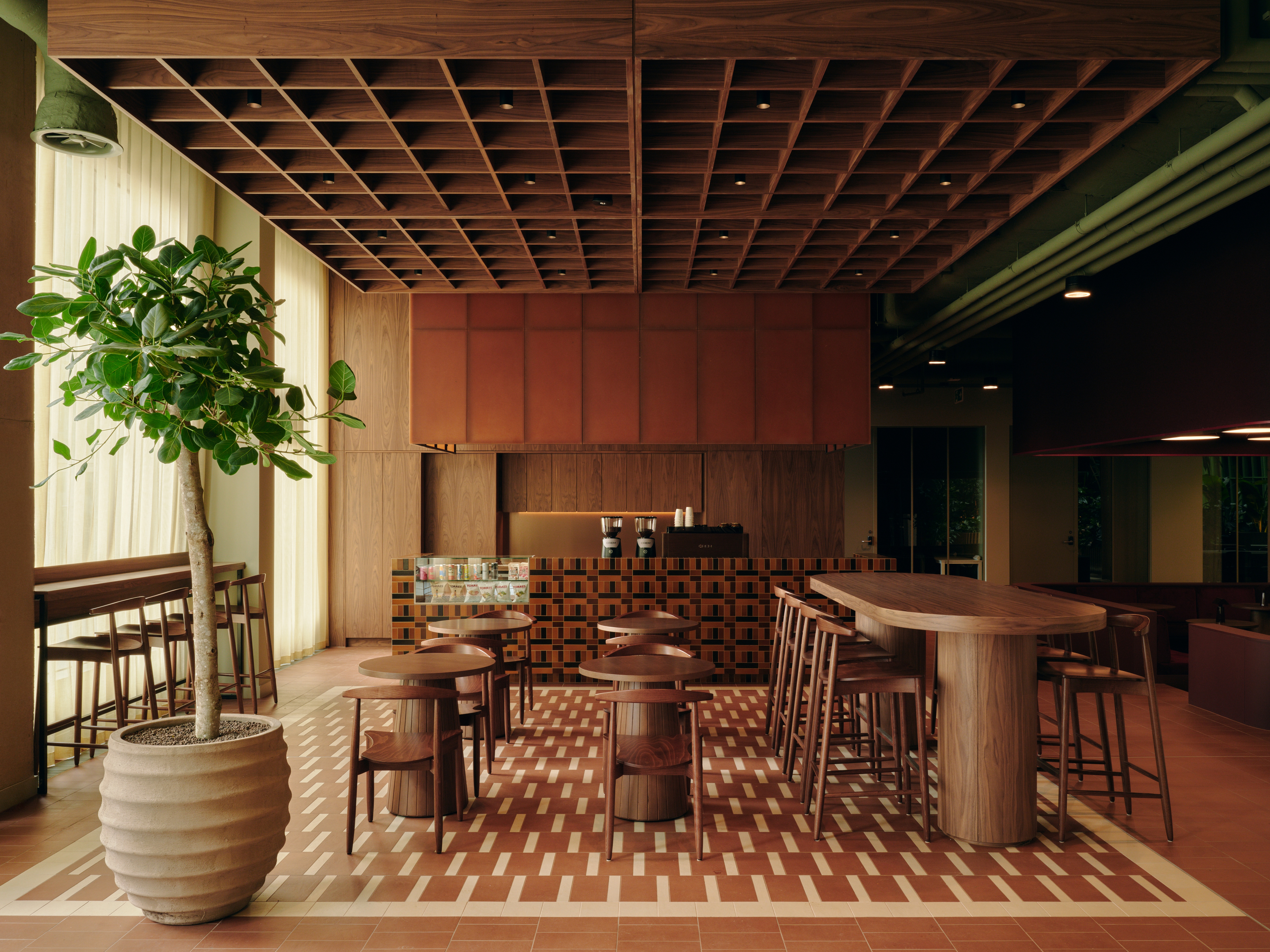 A series of interior shots of a workspace designed with terracotta-hued checkered floors, coffered ceilings in wood and back-lit blocks, pendant, see-through lighting, mid-century furniture,