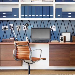 Blue home office with dark wood desk and white shelves organised with blue box files and folders