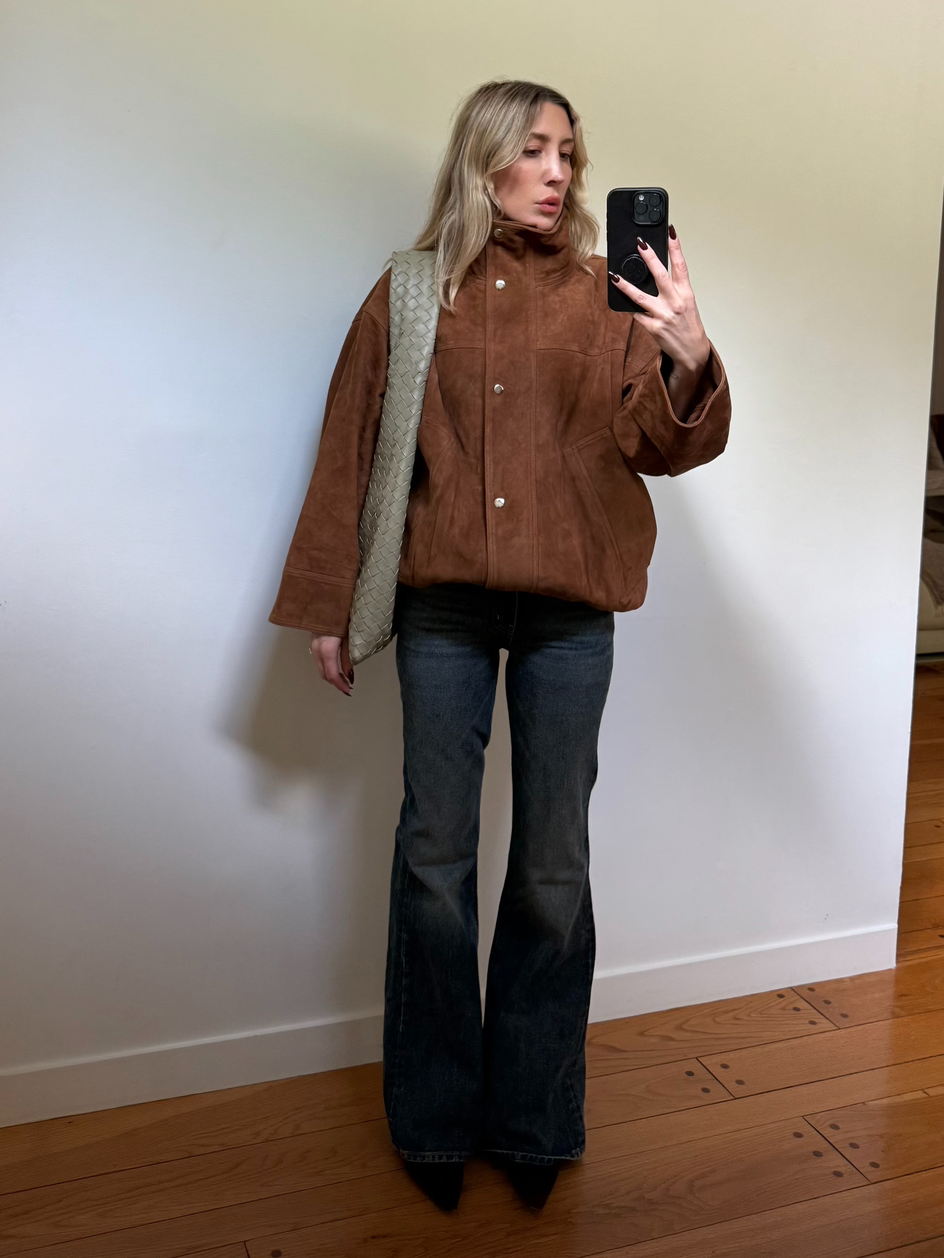 Angela Fink wearing a suede jacket, flared jeans, and a tote bag