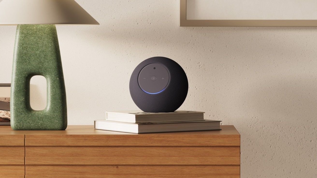 The Amazon Echo Studio with Home Camera sitting beside a lamp on a short shelf in a home.