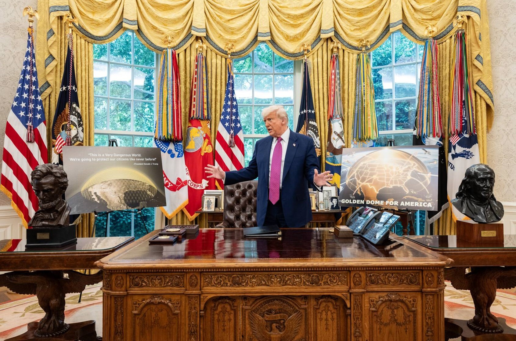 A man wearing a tie stands behind a desk next to posters of illustrations of the Earth covered in a golden orb