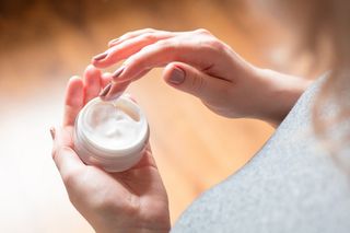 A woman holding a container of skin cream.