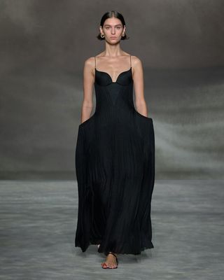 A female model wearing a long sleeveless black dress and sandals.