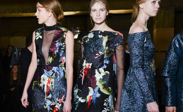 Three women wearing dresses with embroidered floral patterns