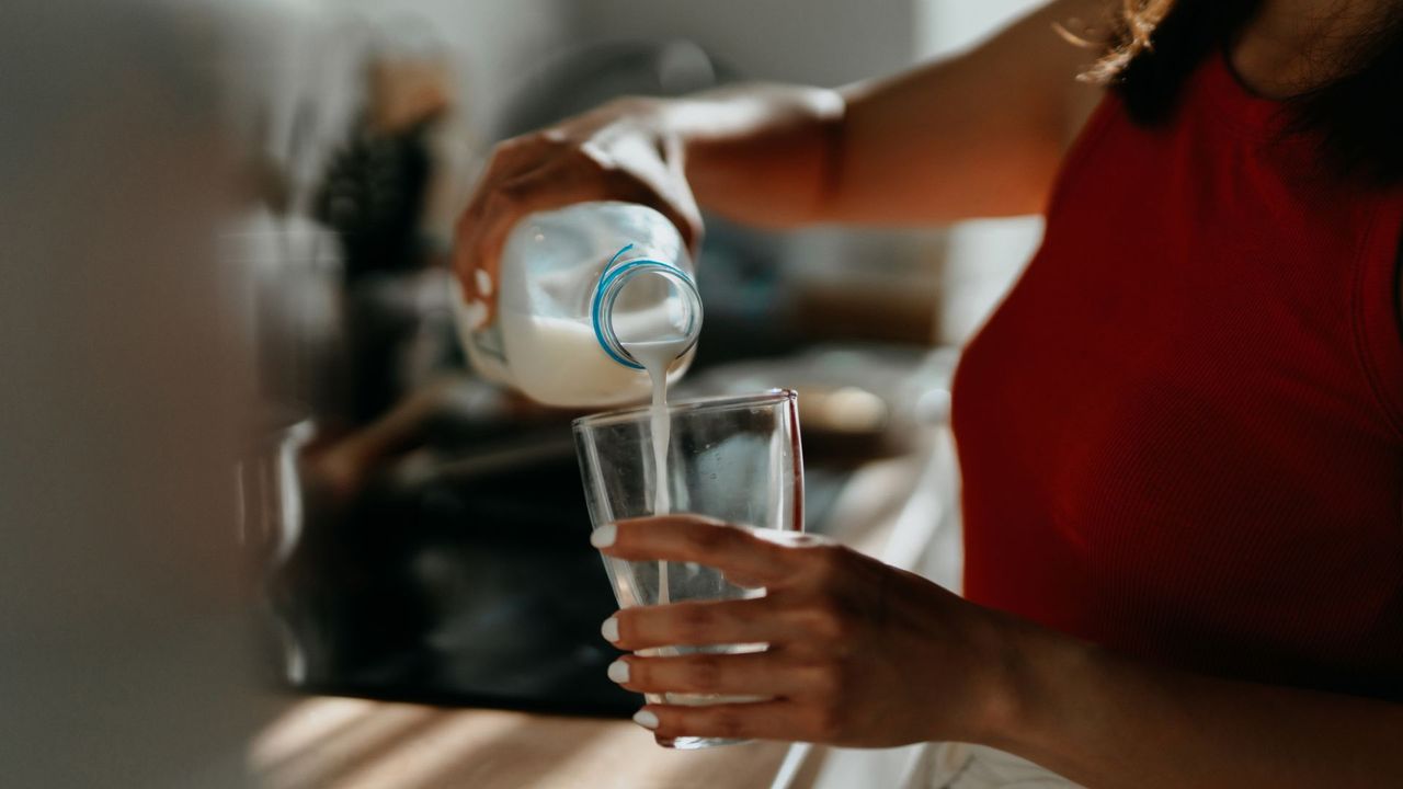 Woman&#039;s hands pouring milk from a bottle into a glass at kitchen counter