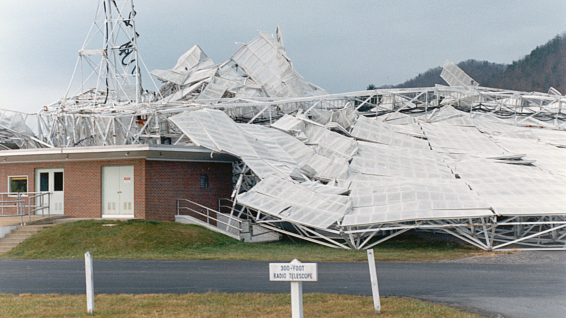 a brick building is dwarfed by the wreckage of a large collapsed structure