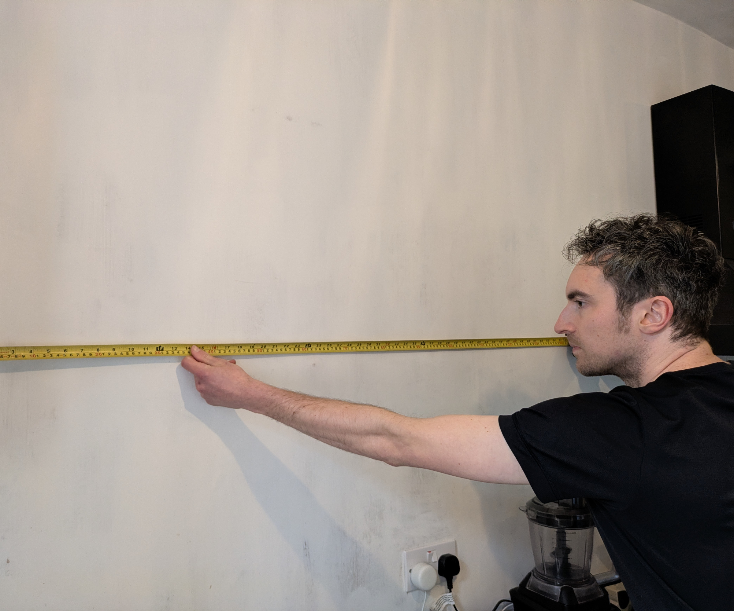 A person holds a tape measure against a wall