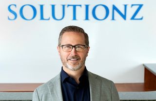 Smiling headshot of Bill Warnick in front of Solutionz logo.