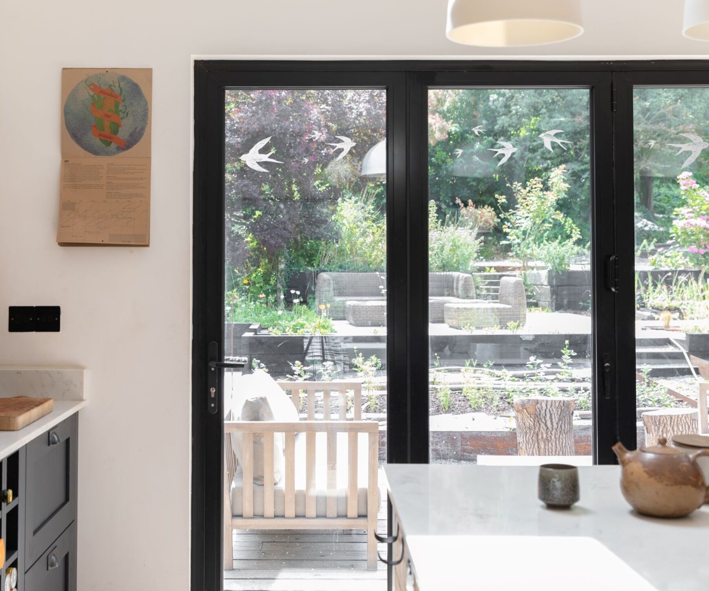Black framed kitchen patio windows with swallow decals overlooking garden