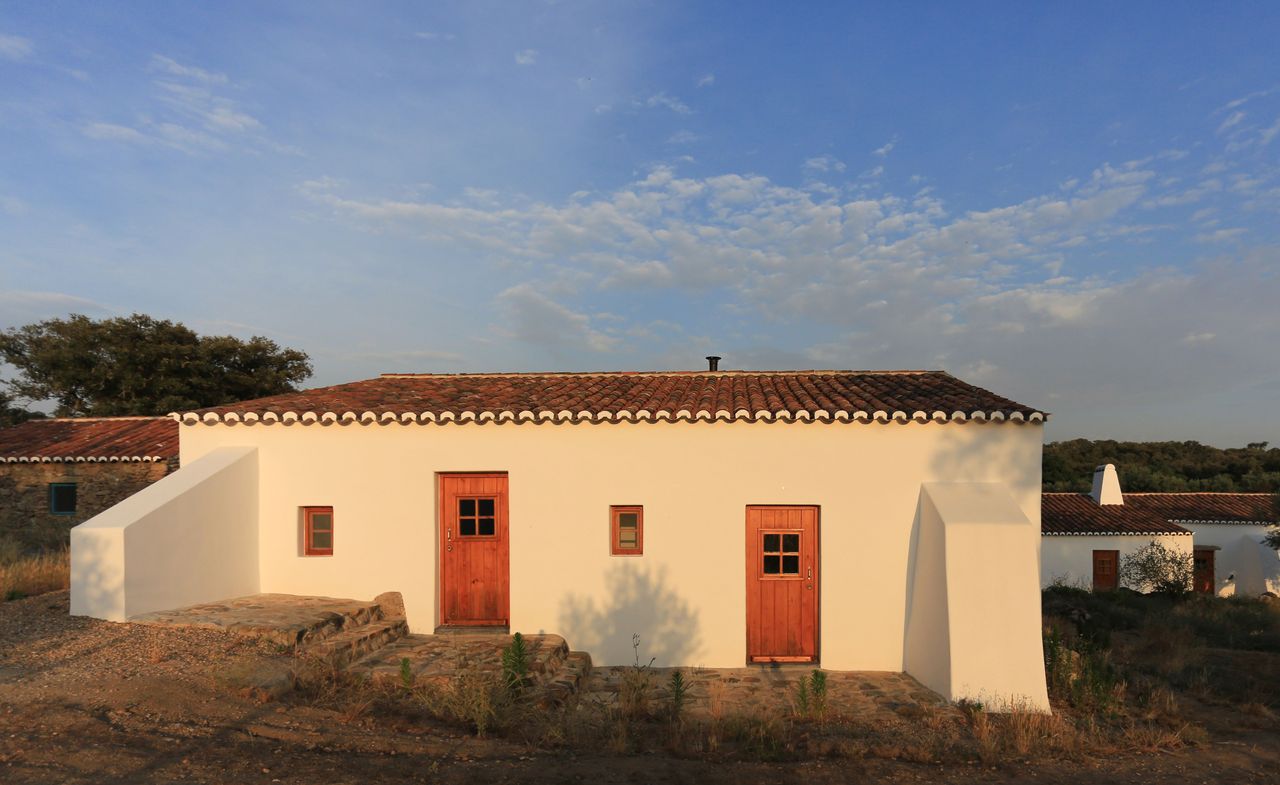 Cream painted house with a red roof as well as two wooden doors and two wooden windows in front of other houses