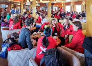 Women in red shirts sit around a table.