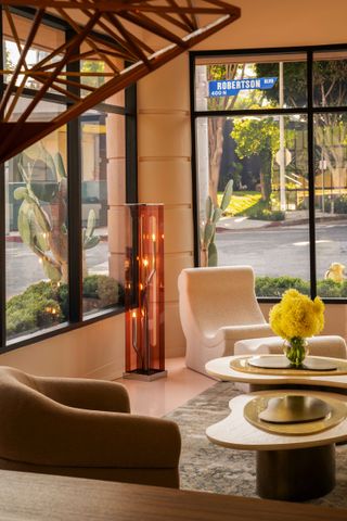 A rose-tinted design showroom features 1970s and 80s-inspired, sculptural furniture such as brass standing pieces, curvilinear coffee tables, and armchairs.