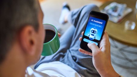Over the shoulder view of man using AI assistant on smartphone while relaxing on sofa