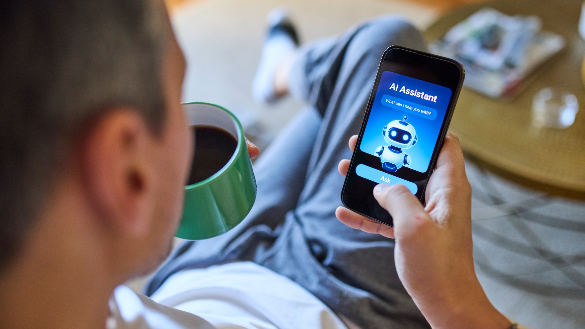 Over the shoulder view of man using AI assistant on smartphone while relaxing on sofa