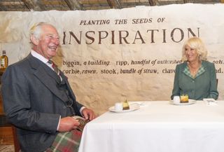 Prince Charles and Duchess Camilla sit laughing at a table in the home of poet Robert Burns.