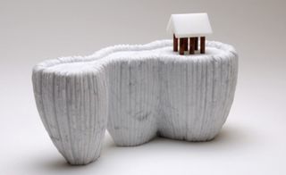 A white marble sculpture represents a tiny house on the cliff.
