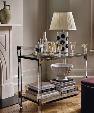 Metal and glass drinks trolley, decorated with table lamp, glassware, books and ornaments