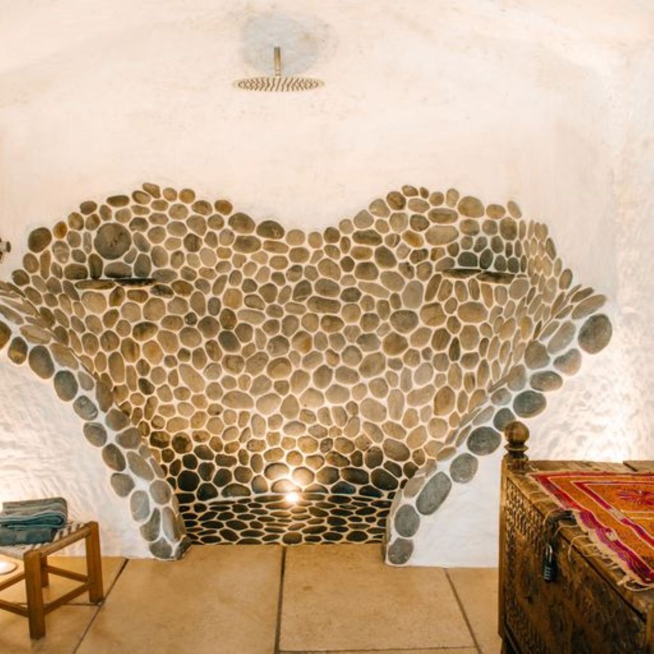 The shower is made from stone with an overhead shower head pointing down for the open plan bathroom which has white stone flooring