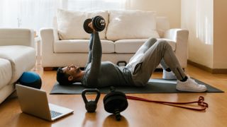 Side view of man working out with weights at home, lying on floor doing chest press