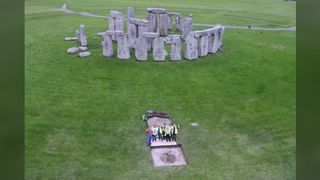 Aerial view of excavation at Aubrey Hole 7 at Stonehenge. A team of archaeologists stand by the hole which is at least 10m away from the circle of Stonehenge.