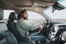 A young, bearded Latino man smiles while driving a luxury SUV.