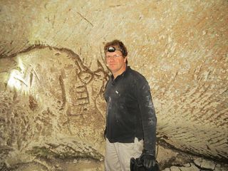 Hiker Ido Meroz stands next to a wall engraving, which appears to depict a key.