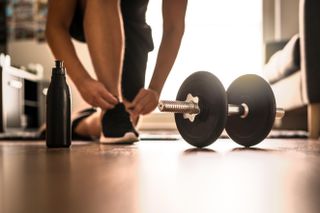 Morning workout routine in home gym. Fitness motivation and muscle training concept. Man in sneakers tying shoelaces in sunlight.