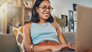 A woman sitting on a sofa facing towards a laptop upon which she's typing