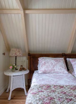 bed under sloping boarded roof with basket work round bedside table and pink toile de jouy bedcovers