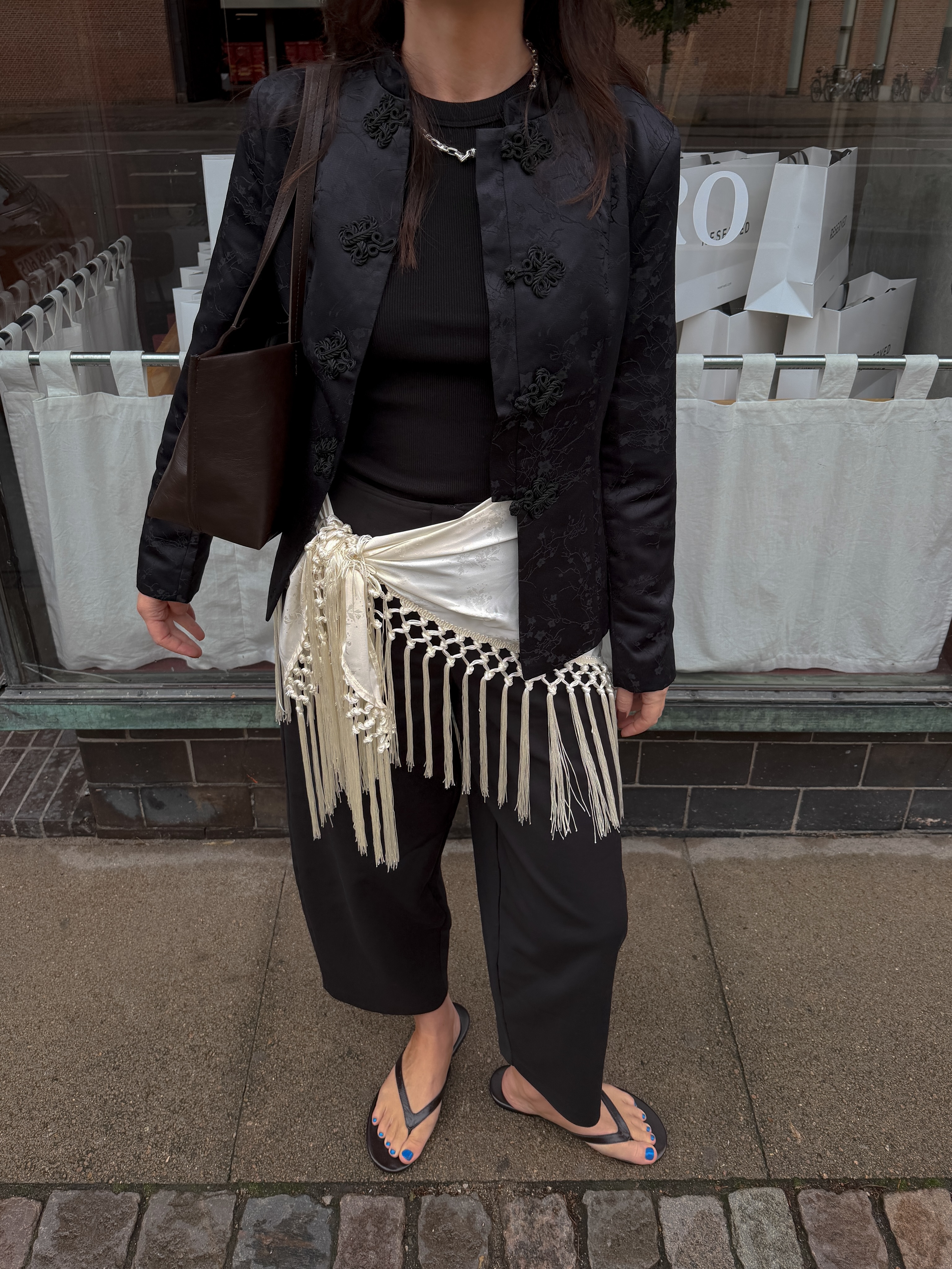 An image of @francescasaffari wearing a frog-tie jacket with a tassel scarf and cigarette trousers.