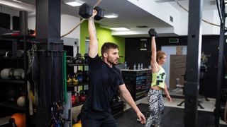 Man and woman perform dumbbell snatch in a gym
