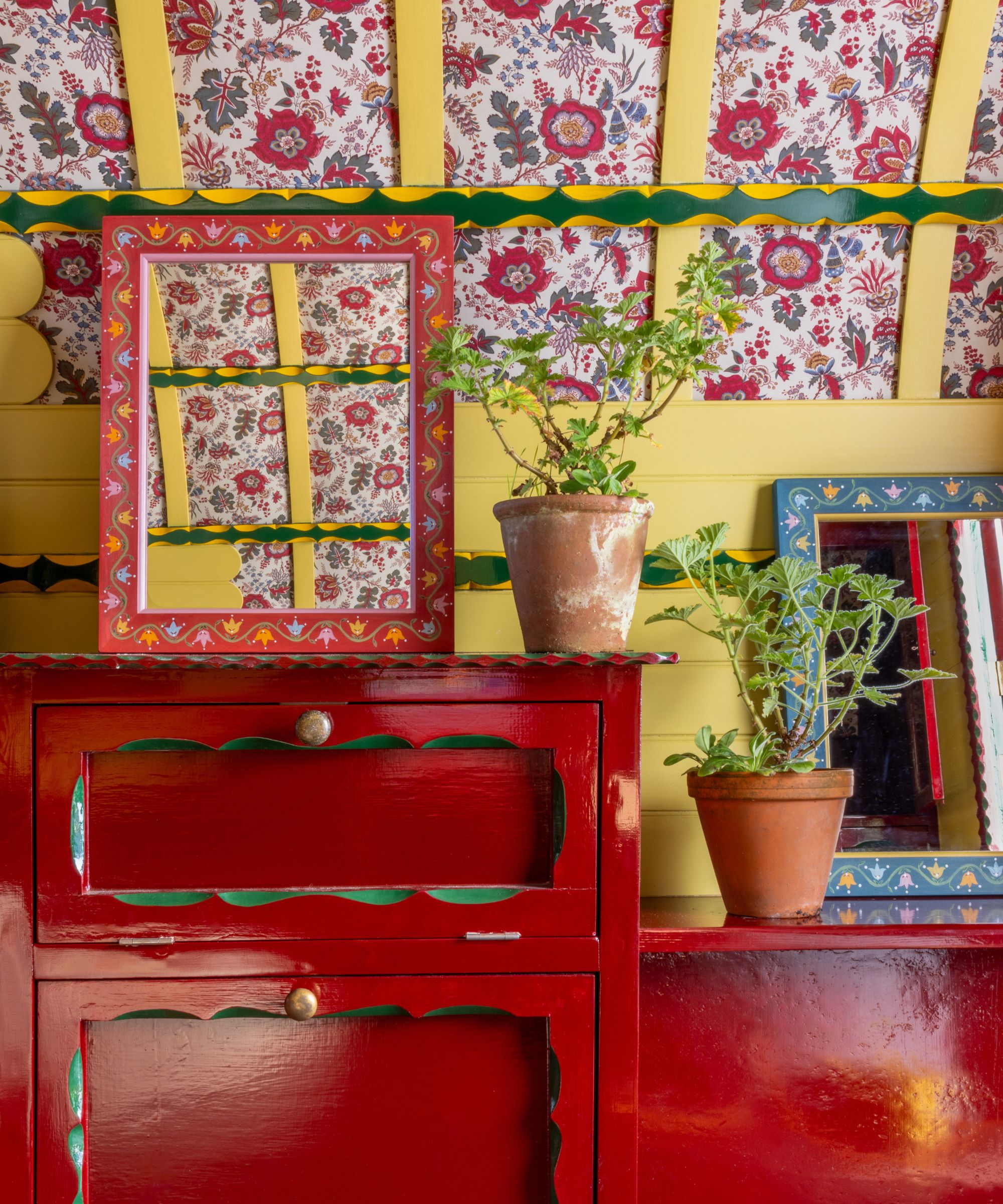 Red side board drawers with folk painted mirrors and yellow wood ceiling