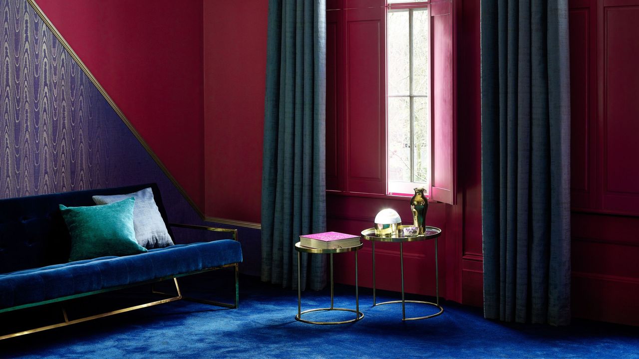 A deep red living room with blue carpet and a velvet blue sofa, with red shutters over the window