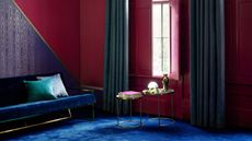 A deep red living room with blue carpet and a velvet blue sofa, with red shutters over the window