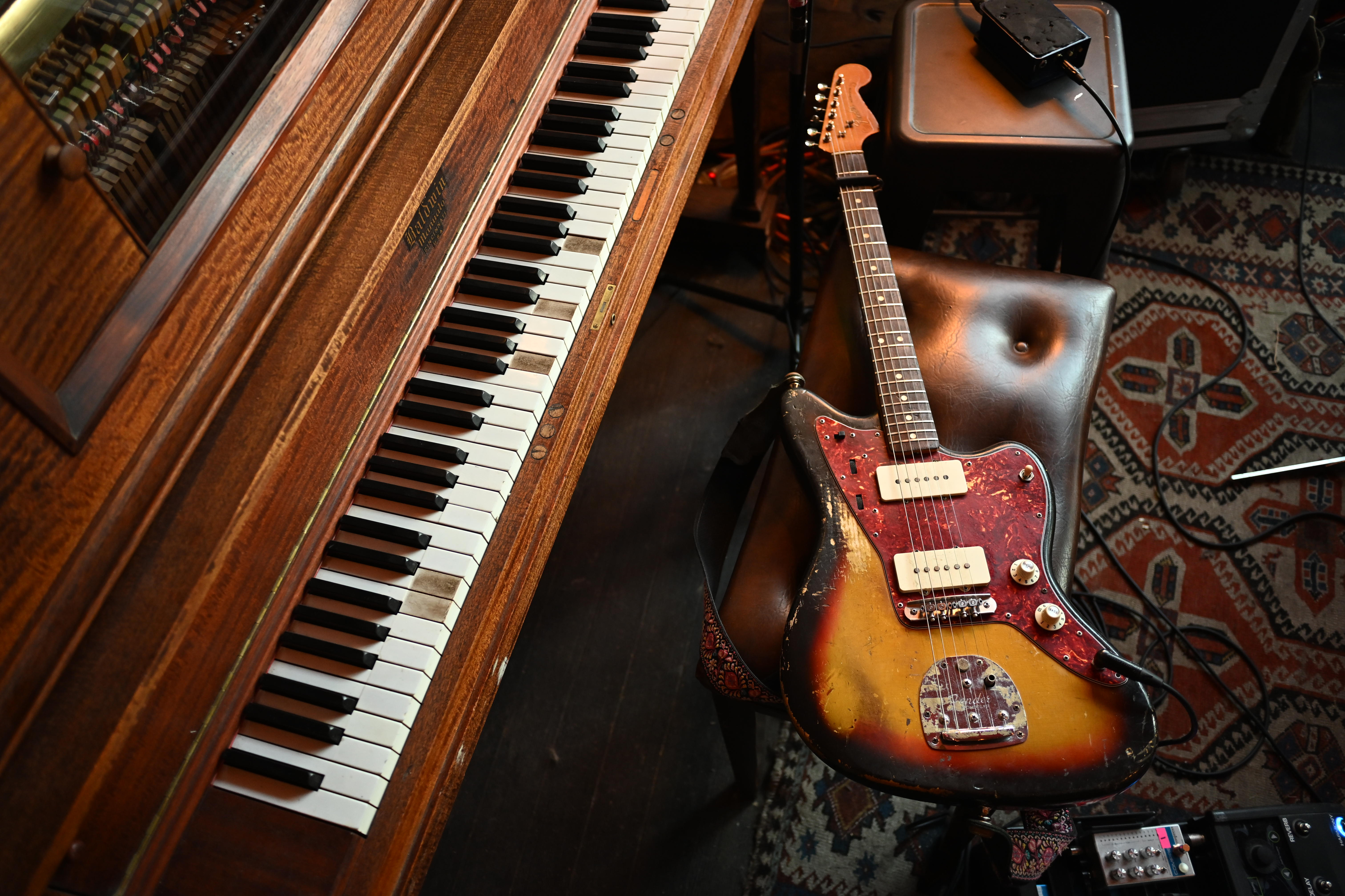 A Fender Jazzmaster guitar and a piano in a home setting