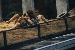 two women wrestle for a ball in a dirt arena, in 'physical 100'
