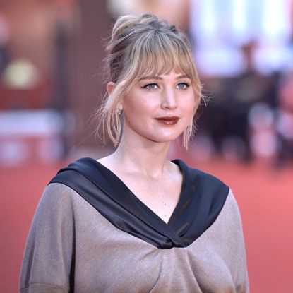 a white woman with blonde hair and bangs posing on a red carpet in front of paparazzi