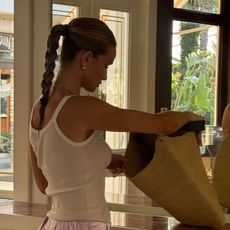 Rosie wears a white tank top, a straw bag, and satin trousers.