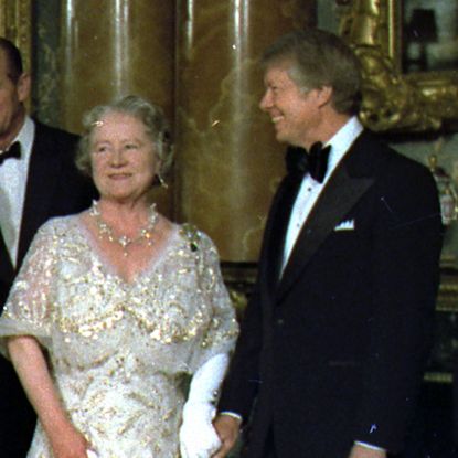 Jimmy Carter wears a tuxedo and holds hands with the Queen Mother, who is wearing a sparkly white and gold gown, alongside Prince Philip, who wears a tuxedo, and Queen Elizabeth II, who wears a bright yellow gown